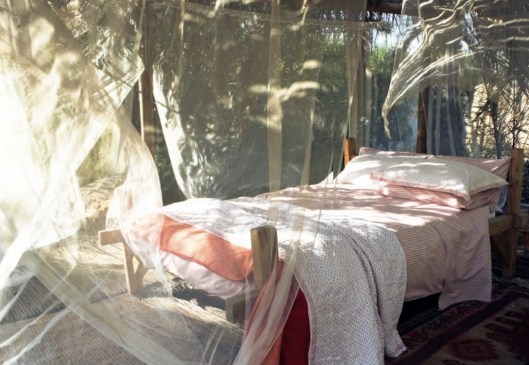outdoor bed with white and pink bedding draped in mosquito netting from spring Toast UL catalogue