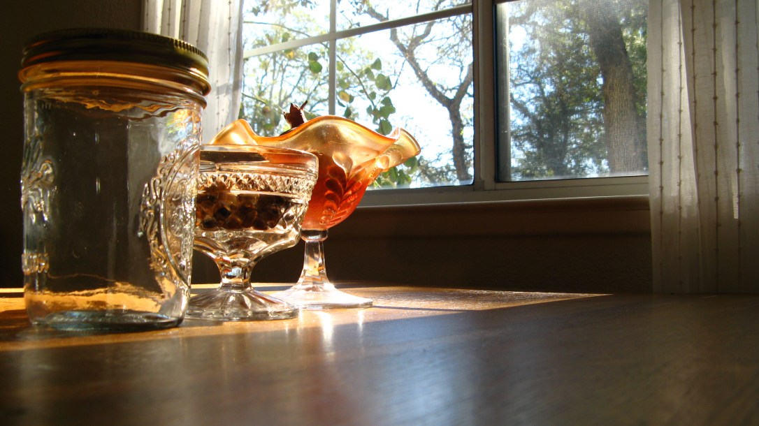 sun shining through window onto wood table with mason jar, crystal ice cream dish, pomegranate and pumpkin seeds - autumn, earth tones, sunshine