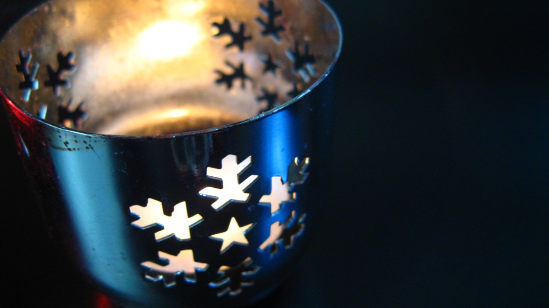 silver metal votive holder with diecut snoflake design - lit with tea light on black background