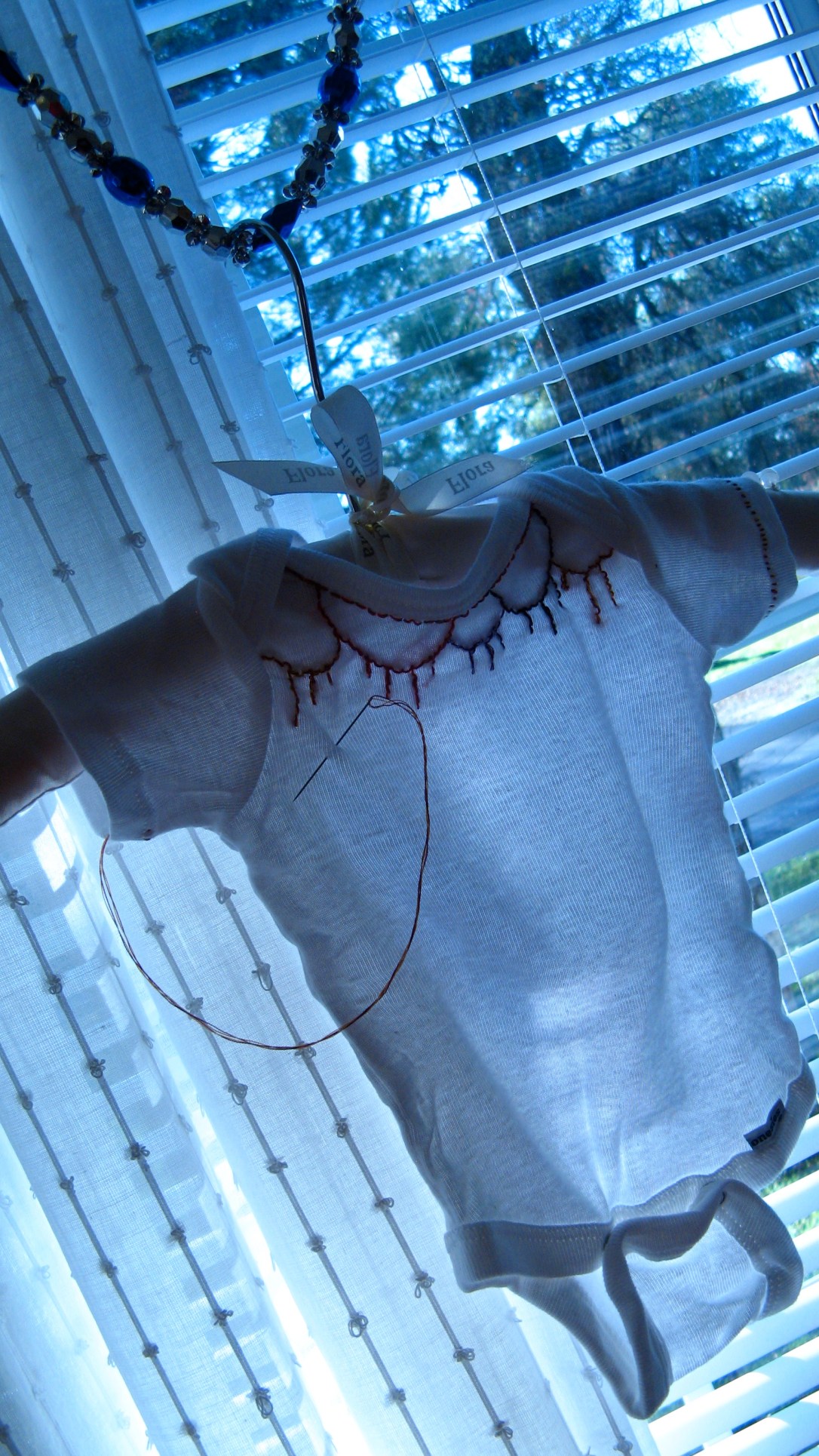 hand-embroidered white baby girl onesie - taken in front of white curtains and blue christmas garland in morning light