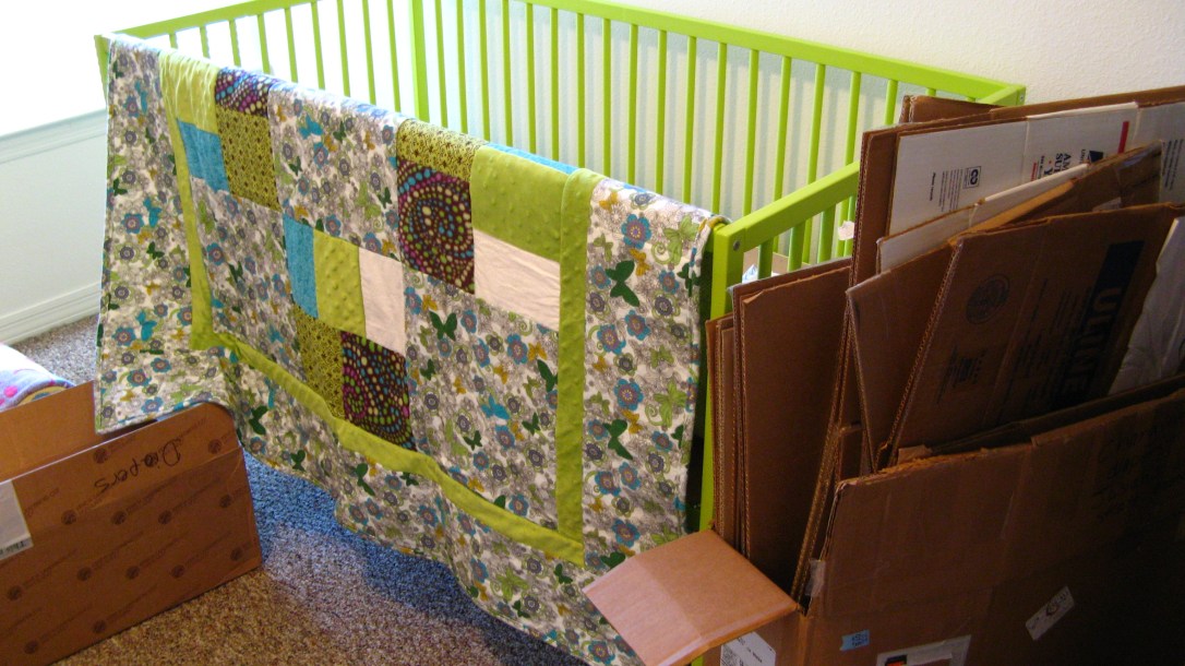lime green IKEA Somnat crib - with handmade quilt and stack of flattened moving boxes nearby