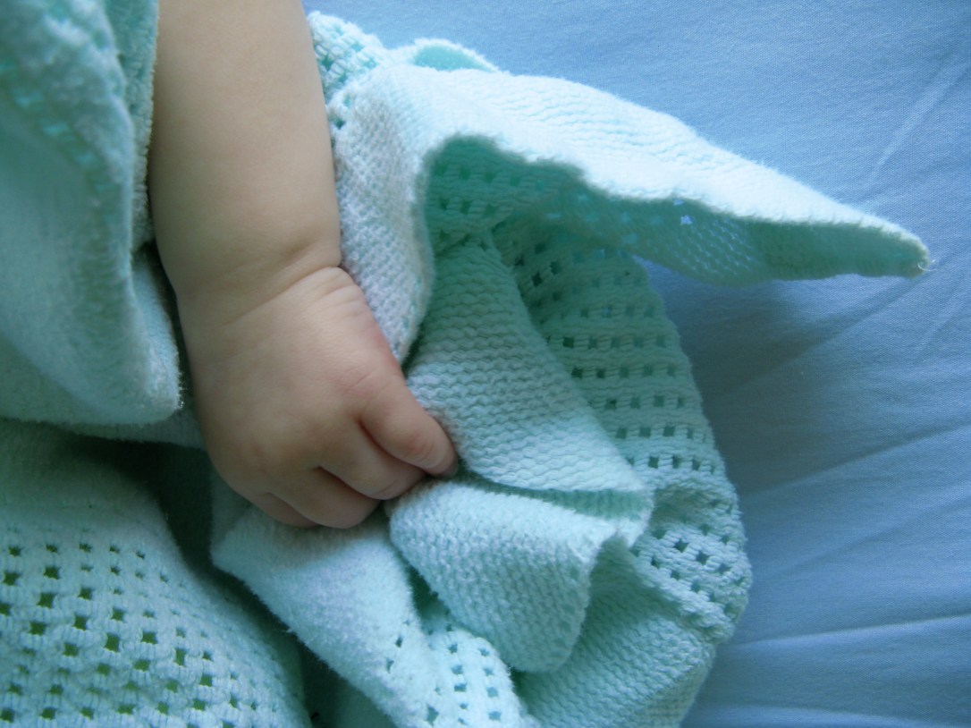 baby hand grasping handful of blanket
