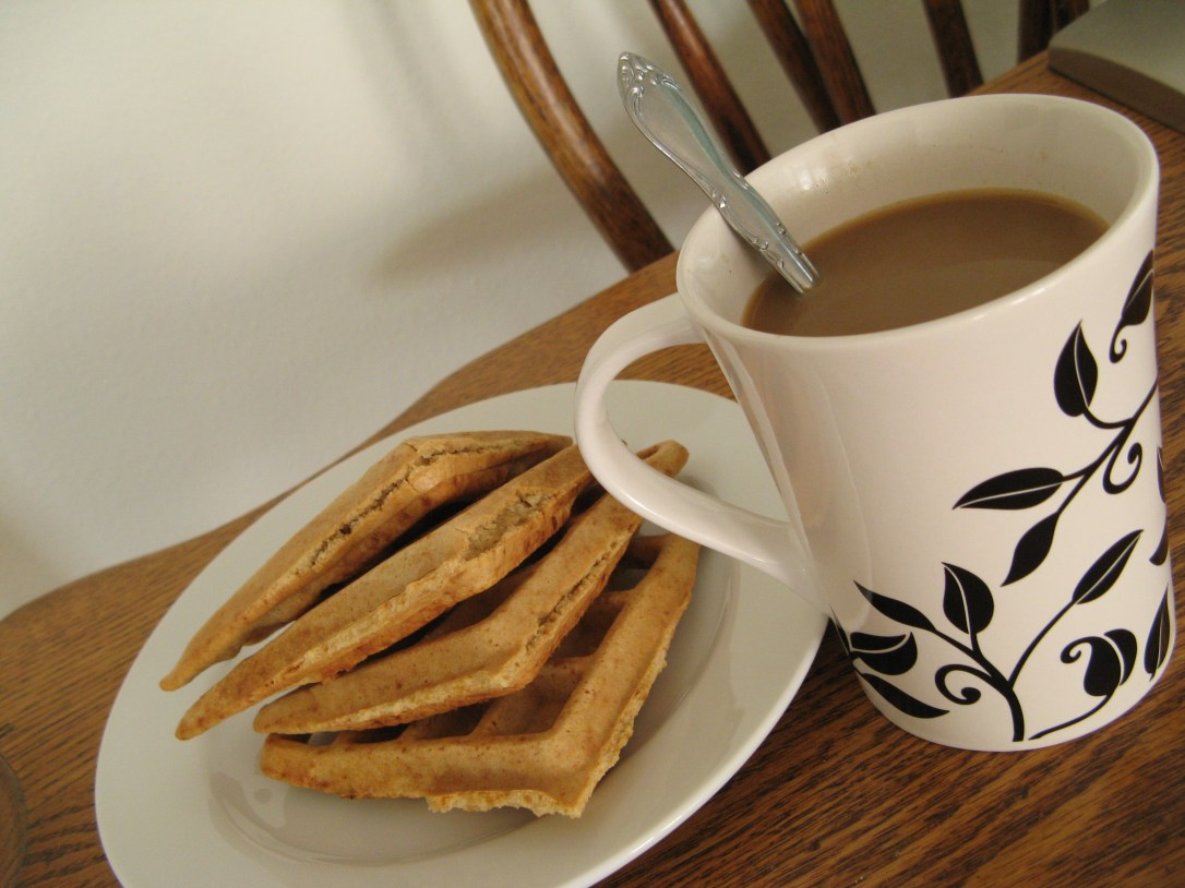 gluten-free waffles on white ceramic plate, coffee in white and black mug, on wooden table