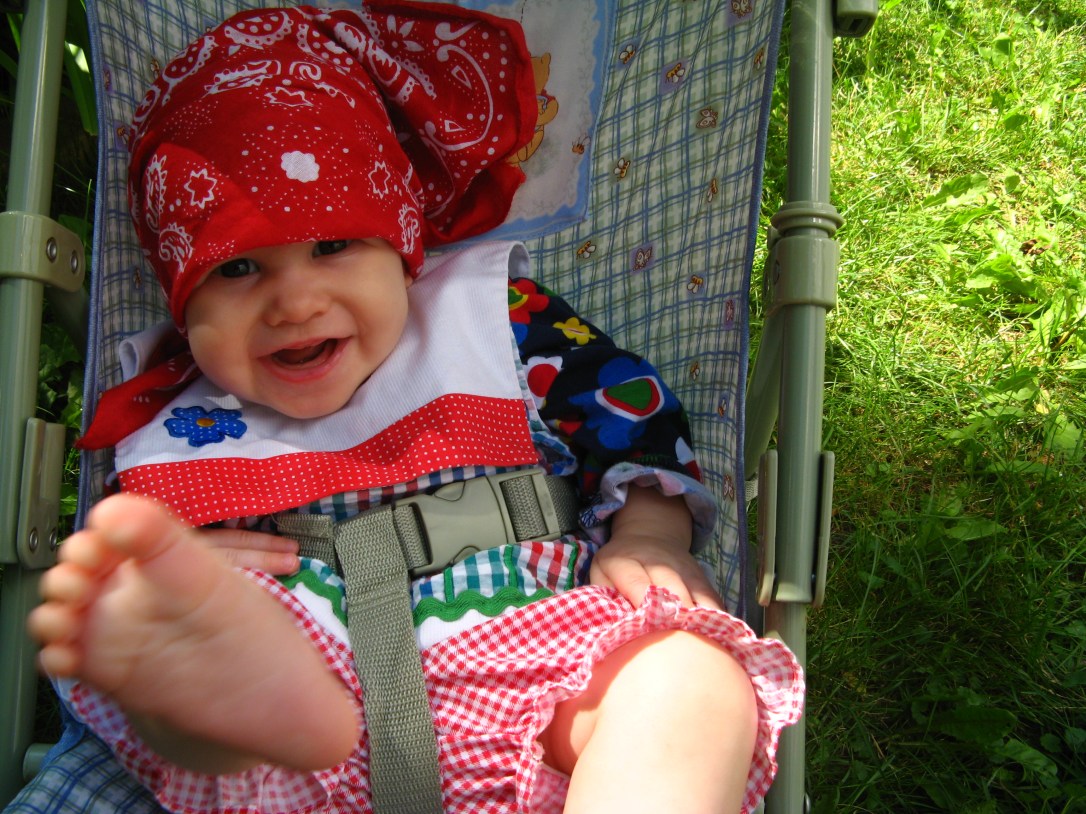 Aveline wearing red bandana and gingham dress, kicking bare foot into camera