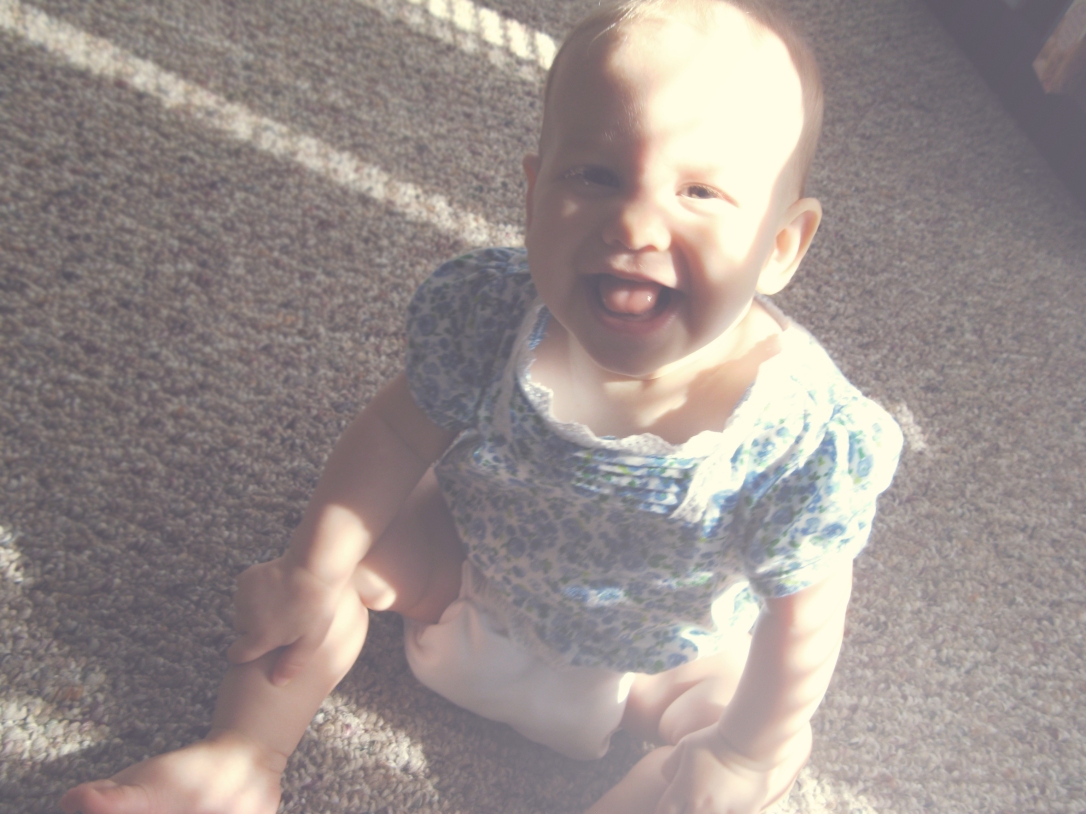 Baby sitting on floor, laughing, in filtered desaturated summer sunlight