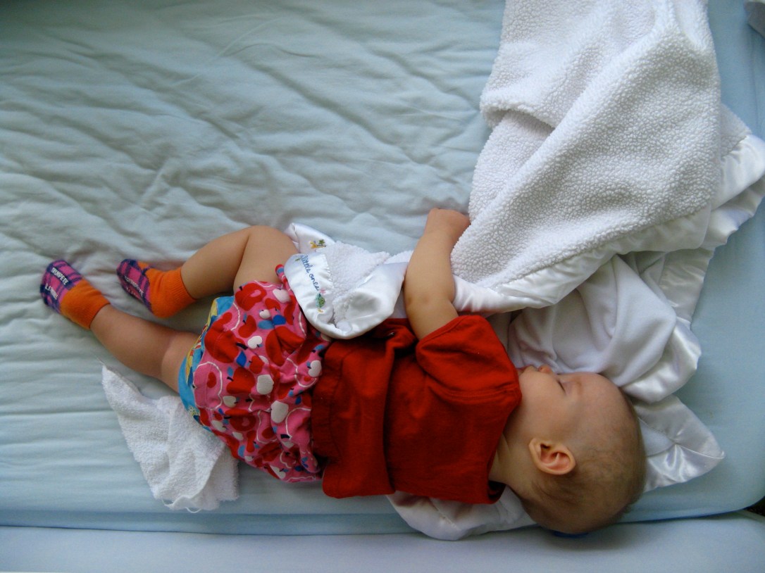 Six month old baby Aveline sleeping peacefully in crib, holding baby blanket, wearing Trumpette socks