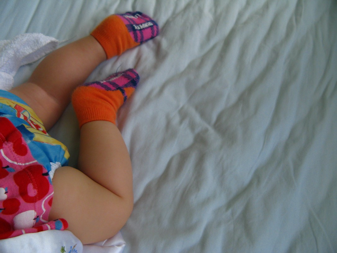 Baby sleeping in crib wearing Bummi cloth diaper cover and Trumpette socks