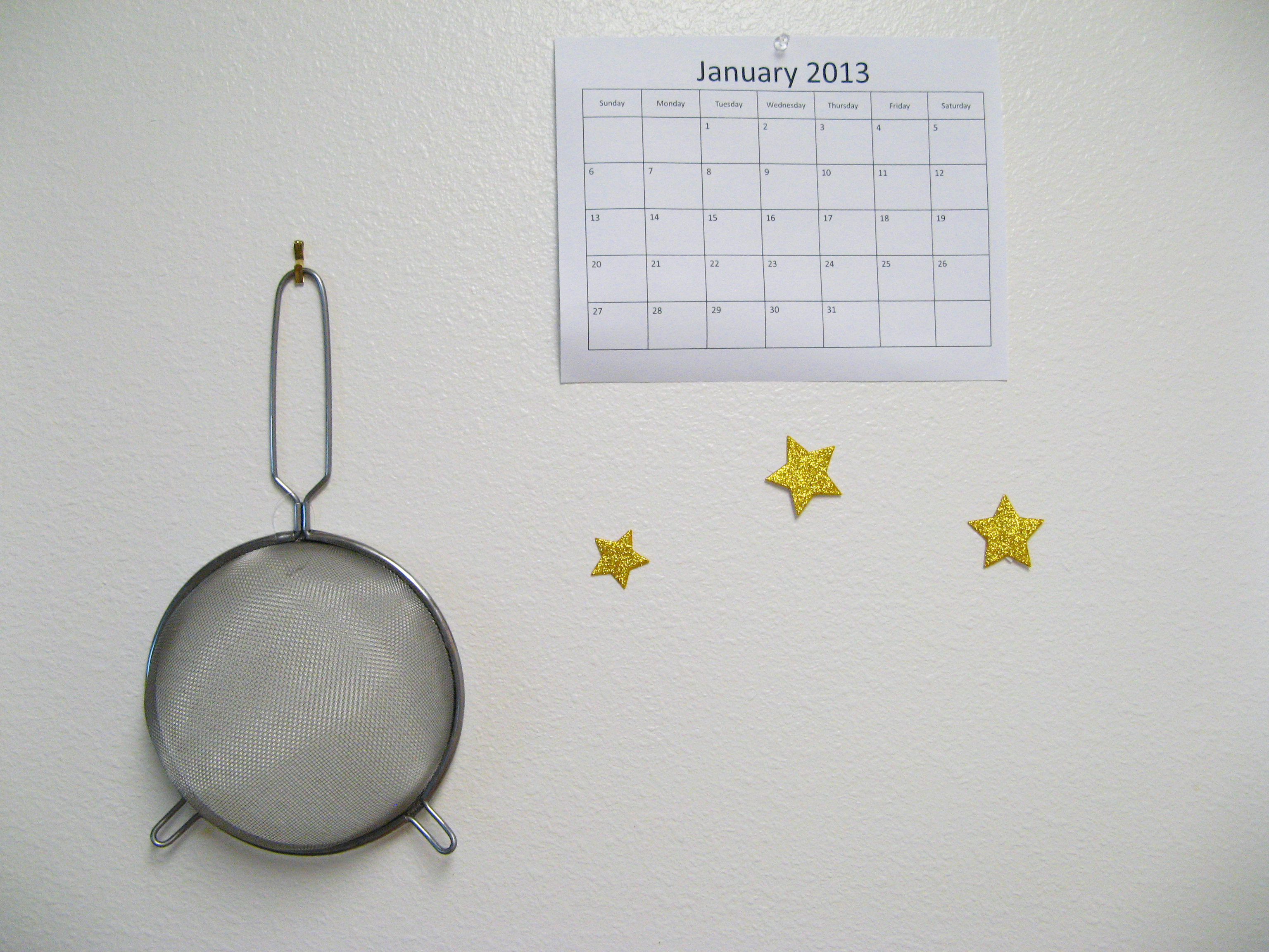 Colander, calendar, and stars on white kitchen wall - photo via Oaxaacborn dot com