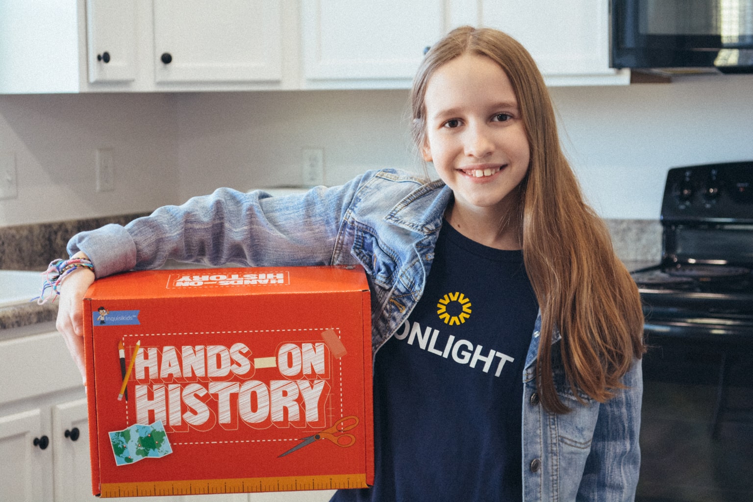 A homeschool student wearing a Sonlight tshirt holds a Hands-on History box from Sonlight curriculum 