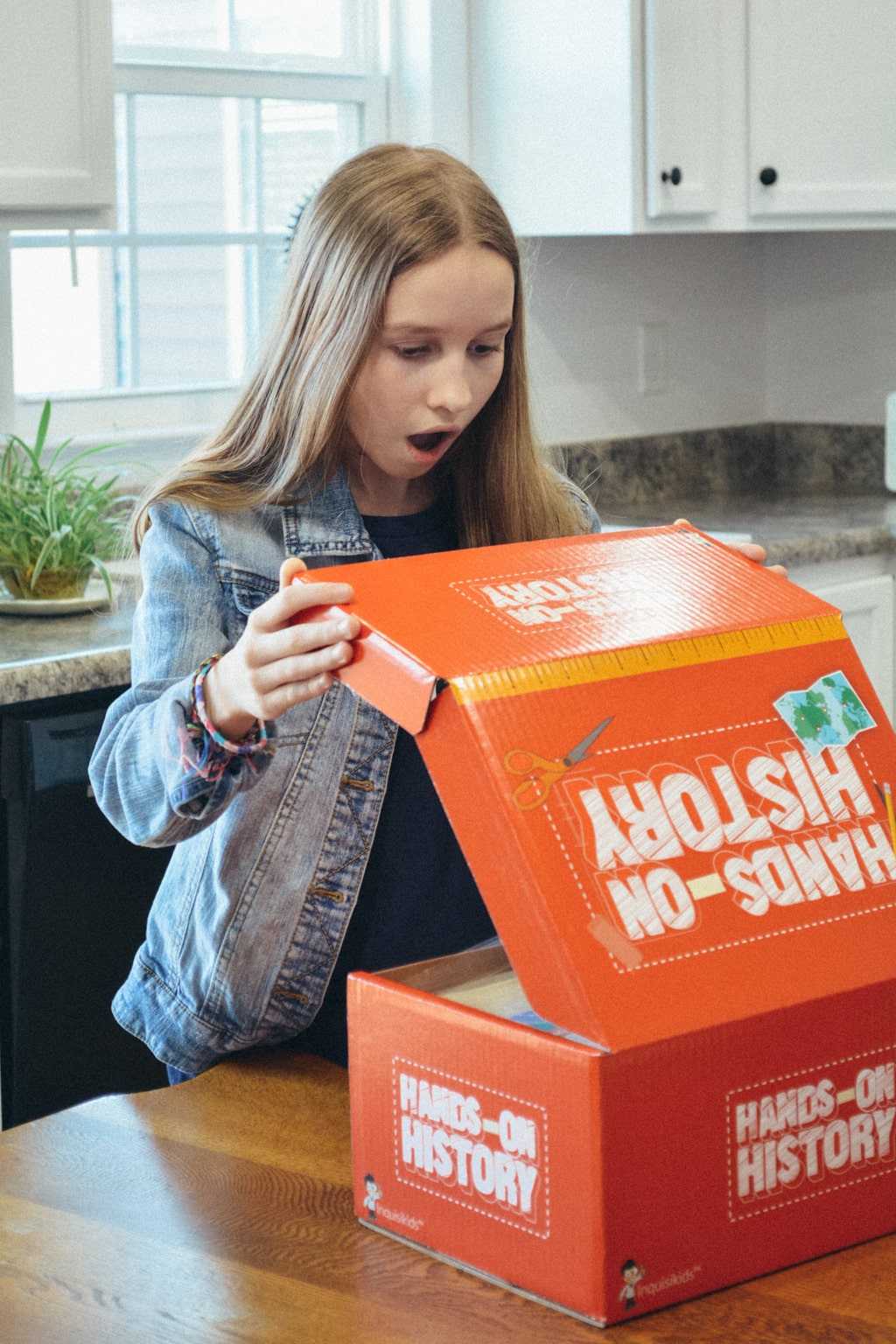 A surprised homeschool student looks inside a Hands-on History project box from Sonlight Curriculum 