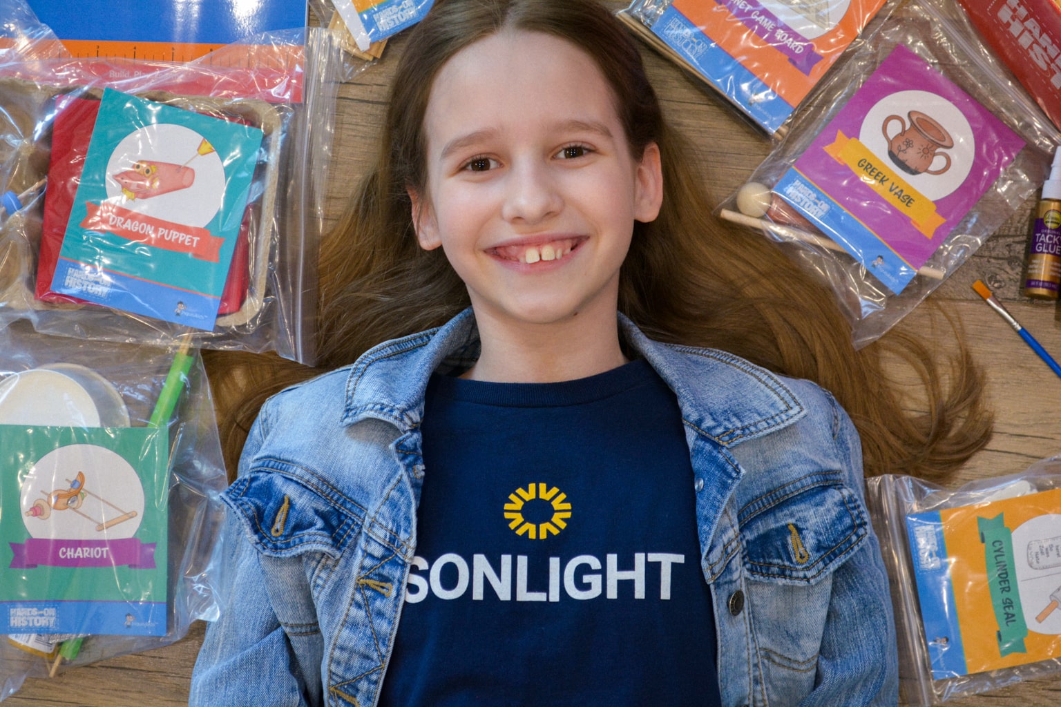 A homeschool student in a Sonlight shirt with prepackaged world history craft activity kits from the Hands-on History project box 