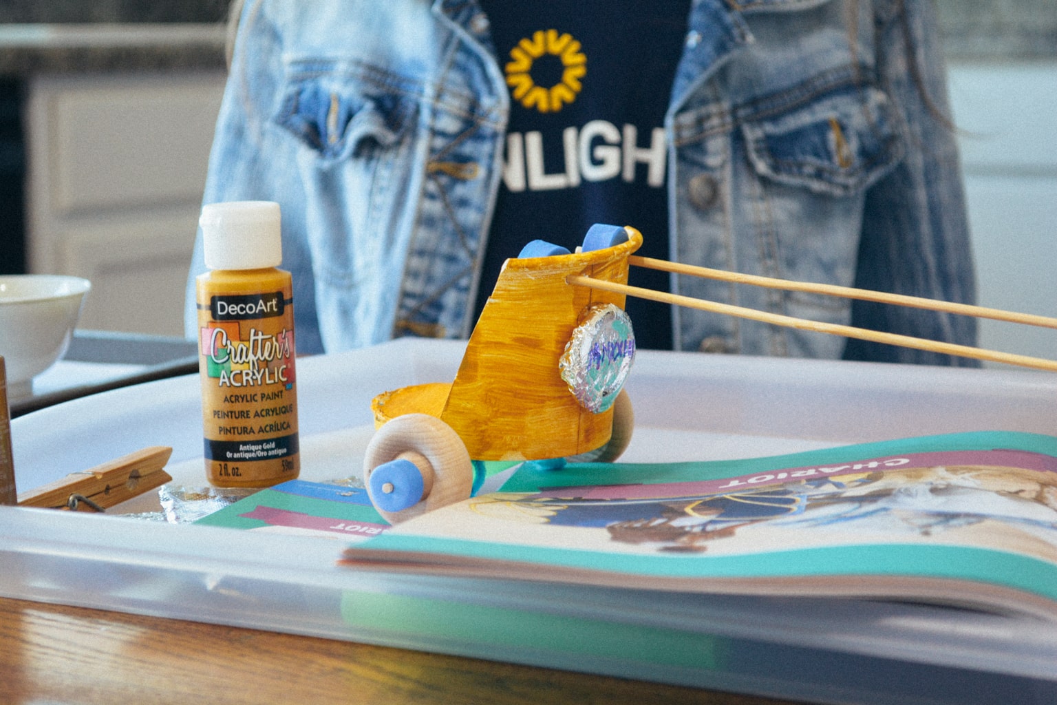 A student sits at a table. She is wearing a Sonlight shirt. There is a tray on the table containing art supplies and a model of roman chariot from Sonlight's Hands-on History project boxes.
