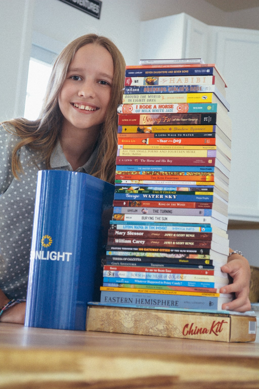 Homeschool student at table with Sonlight's big blue binder and tall stack of homeschool curriculum from Level F