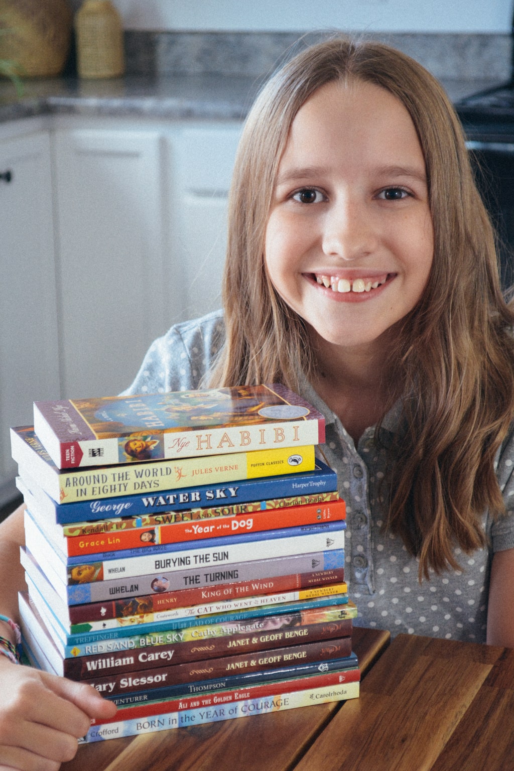 A smiling homeschool student sits next to a stack of Sonlight books.