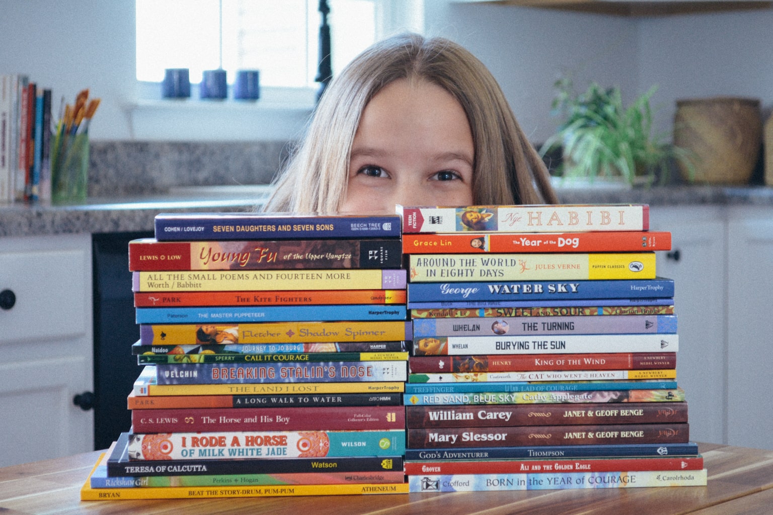 Homeschool student smiles behind two stacks of diverse middle grade novels from Sonlight Curriculum's Level F Eastern Hemisphere studies