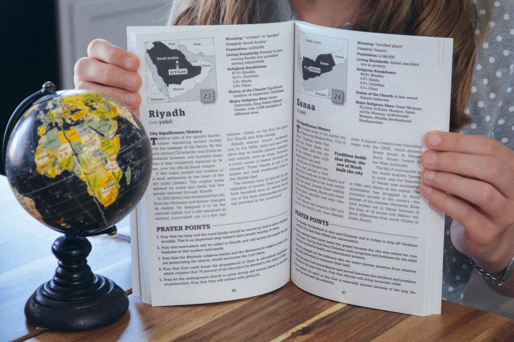 Homeschool student holding open a two-page spread of Praying Through the 100 Gateway Cities of the 10/40 Window