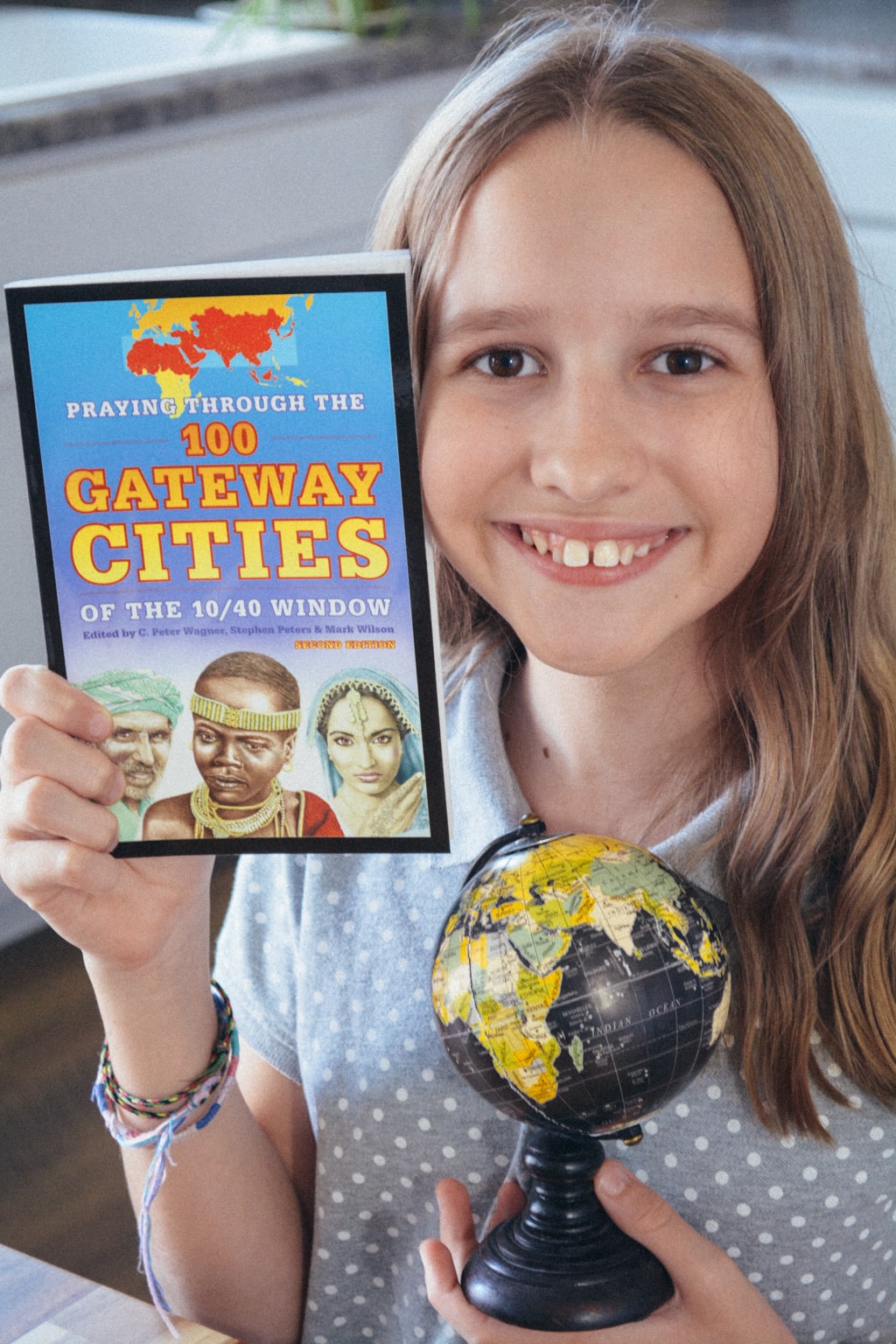 Homeschool student holding a small black globe and a copy of Praying Through the 100 Gateway Cities of the 10/40 Window