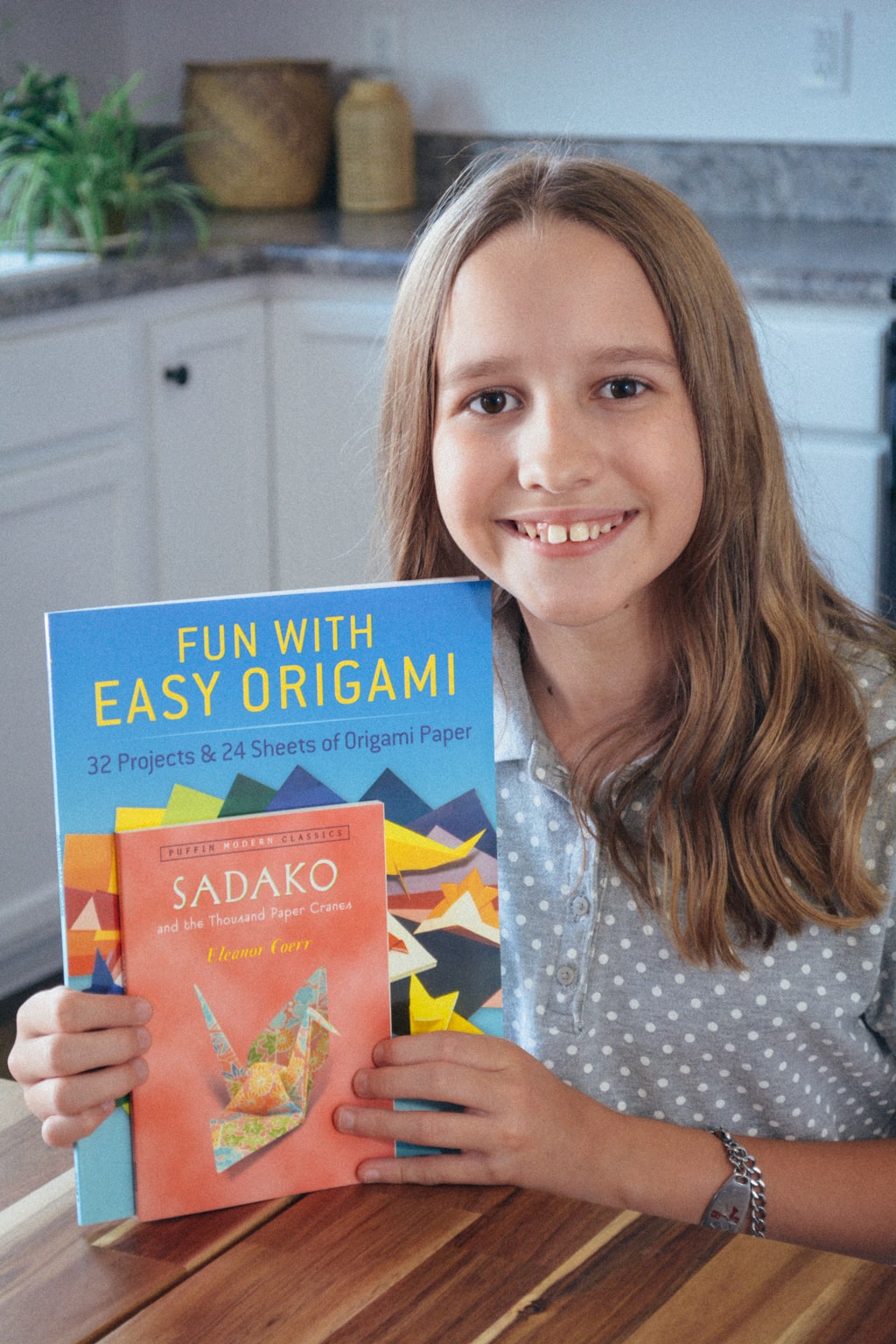 Homeschool student holds up Fun with Easy Origami and Sadako & the Thousand Paper Cranes, both part of the hands-on components in History / Bible / Literature F from Sonlight Curriuclum.