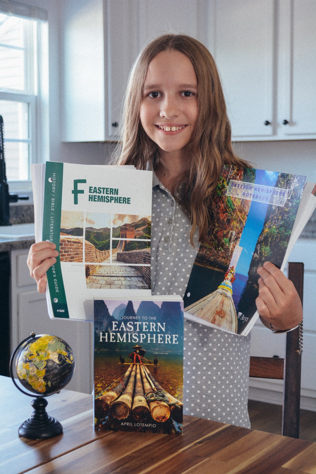 Homeschool students stands at table near a globe and holds Sonlight Curriculum's Eastern Hemisphere materials.